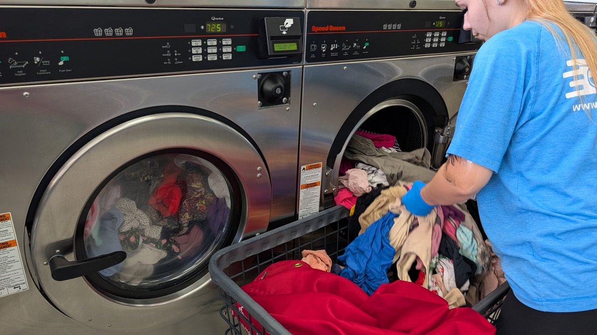 Attendant loading laundry from a cart into a Speed Queen washer