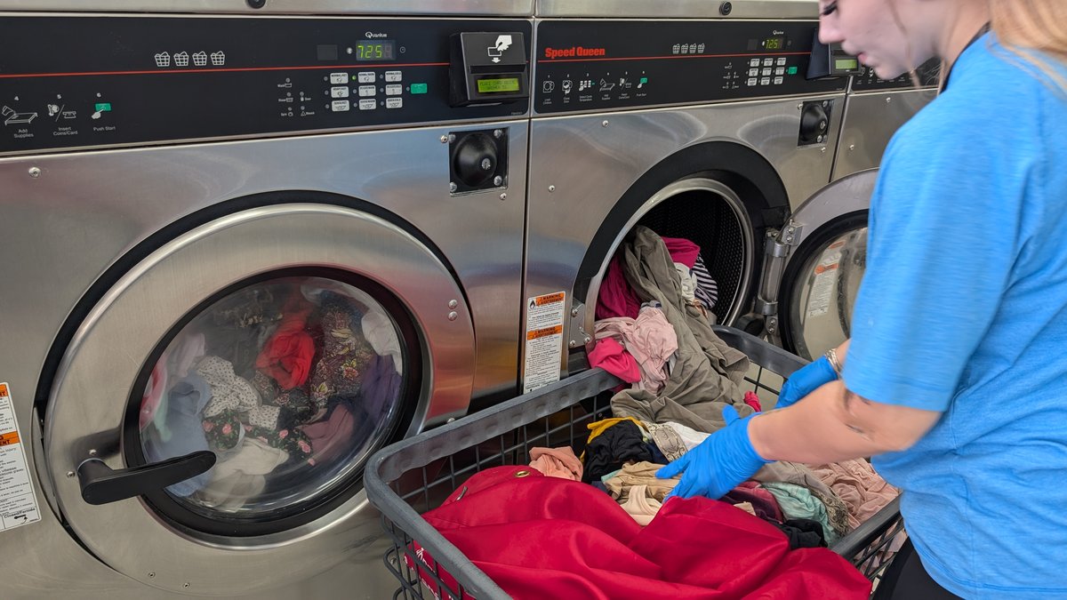 Attendant in gloves loading a wash and fold order into a Speed Queen washer