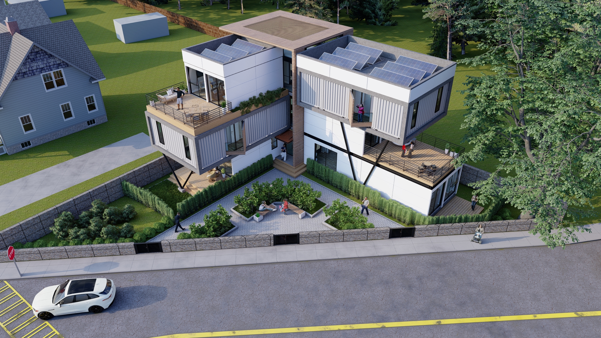 Modern three-story shipping container building with cantilevered upper sections featuring large windows and solar panels on the flat roofs, surrounded by a fenced garden with greenery and seating area, people on balconies and near entrances, next to a paved street with a white car parked and a person pushing a stroller on the sidewalk.