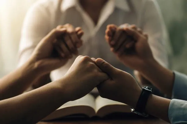 Hands joined in prayer over an open book