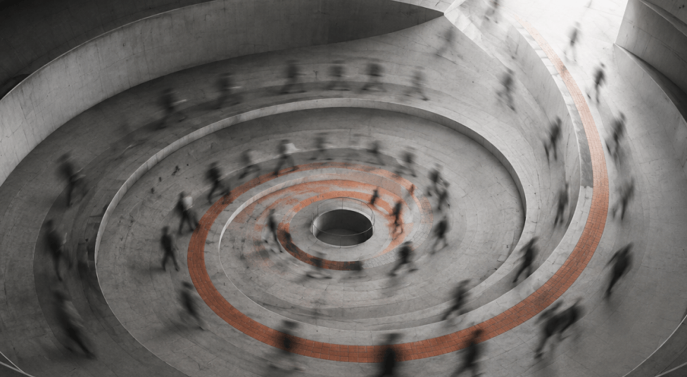 Blurred people walking along a spiraling ramp inside a cylindrical concrete structure with a central circular opening.