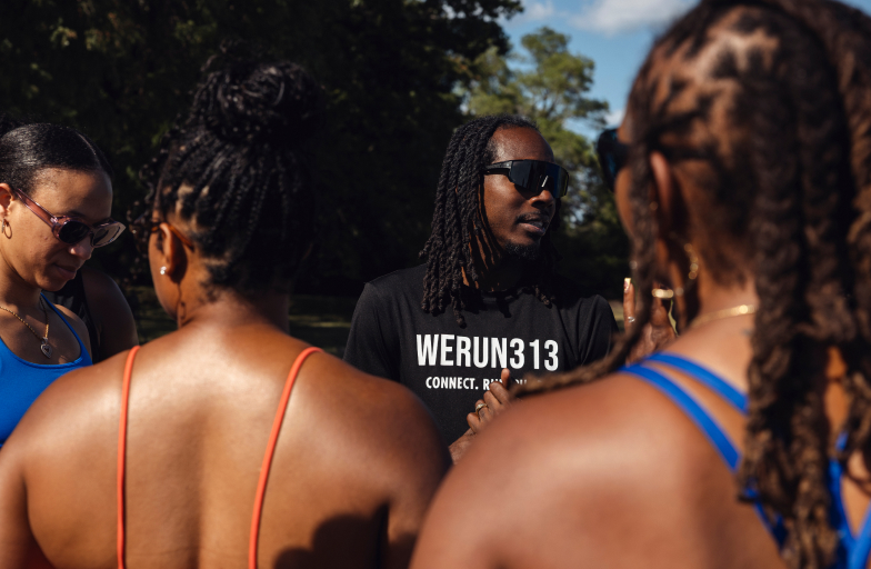 The backs of two women facing a man wearing sunglasses and a black shirt that says "We Run 313."