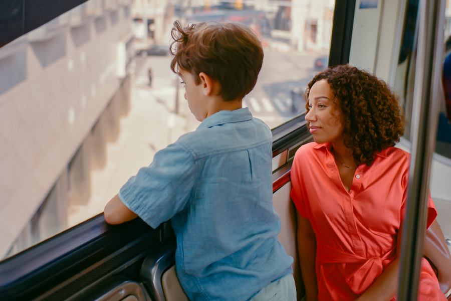 Woman in an orange dress sitting on a train with a young boy in a blue shirt who is looking out the window.