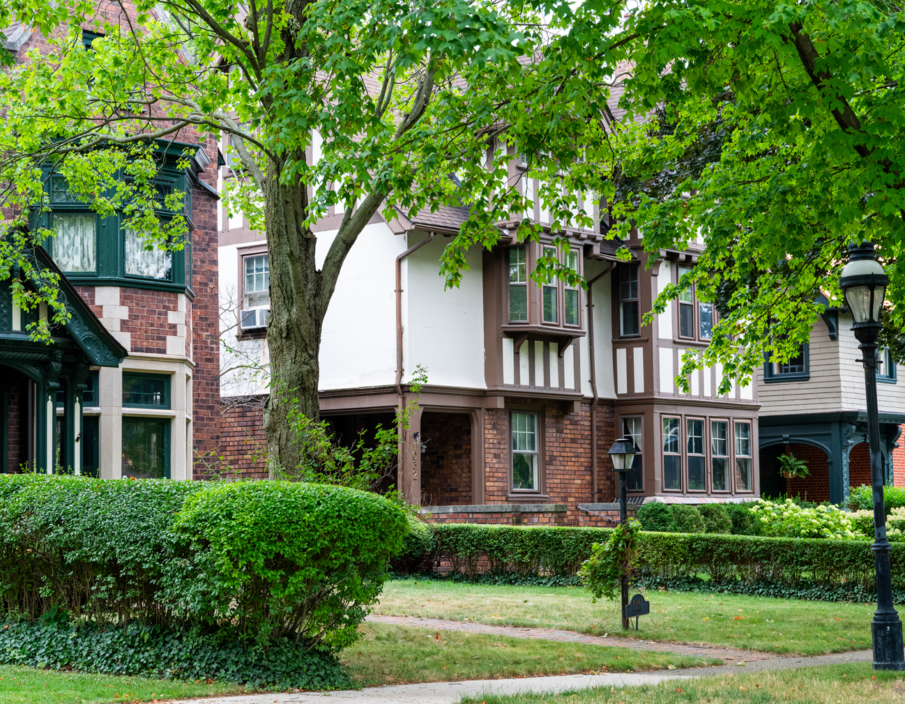 Photo of a white and red brick historic house partially hidden behind a large tree.