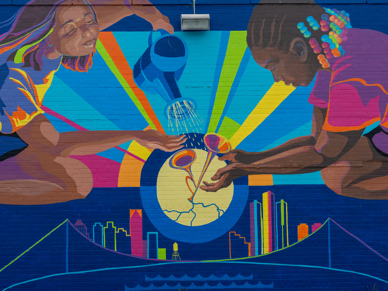 Photo of a brick wall with an abstract mural featuring two children watering instruments with the Detroit skyline below.