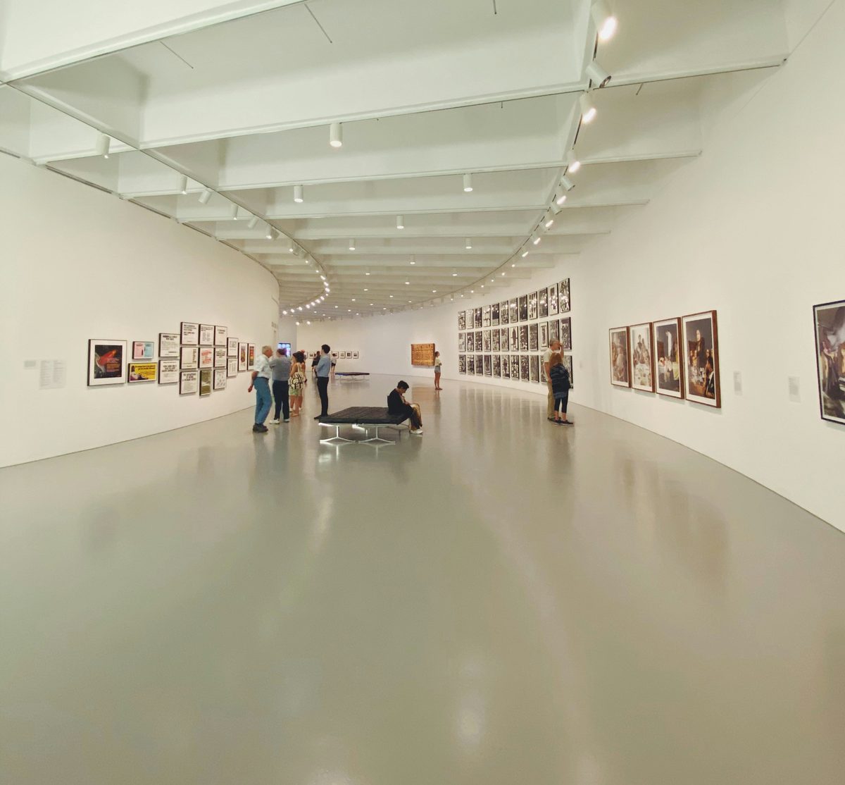 A visitor standing at the far end of a pale gallery wall hung with paintings