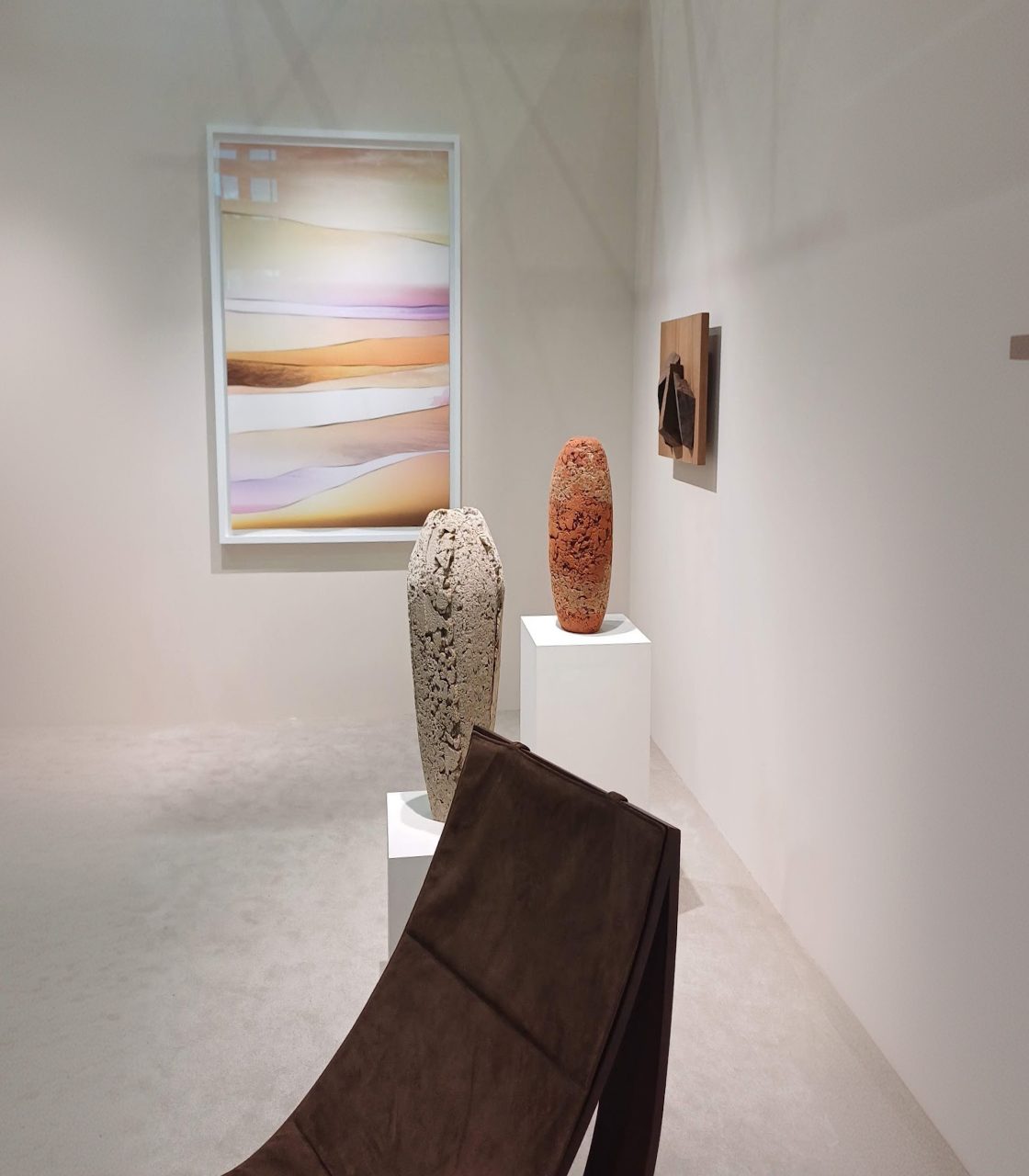 A quiet gallery room with a framed abstract, two ceramic vessels and a leather lounge chair