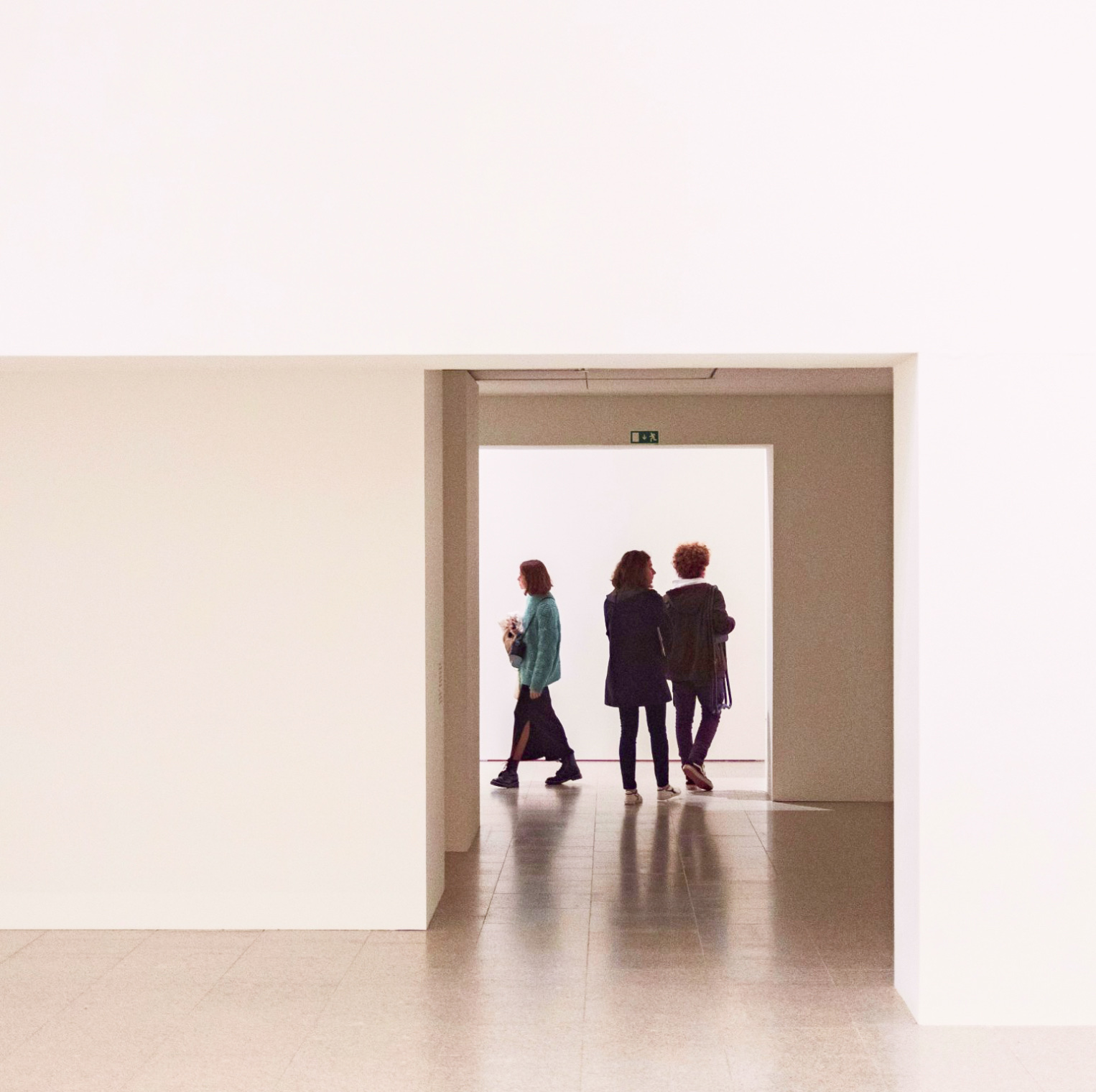 Three people walking together through a doorway in a bright white gallery