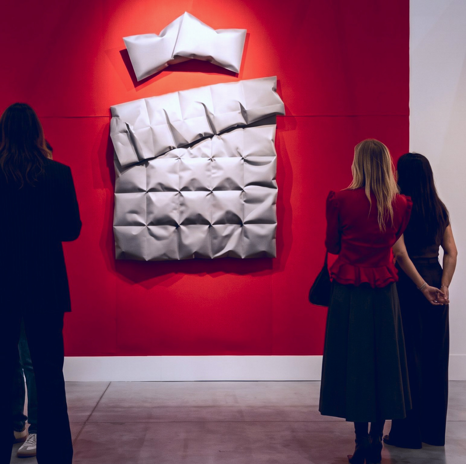 Visitors in front of a folded white relief on a red gallery wall