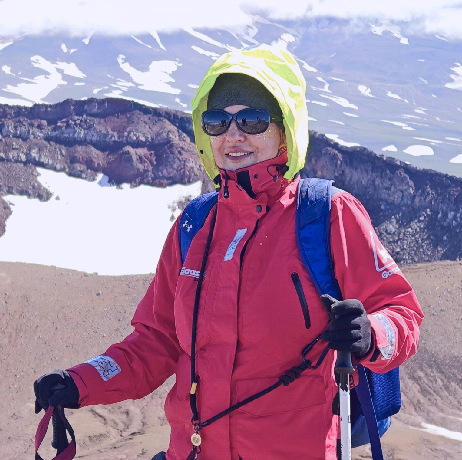 Elena Vysotskaia on a volcanic ridge in a red jacket, with snowfields and cloud behind her