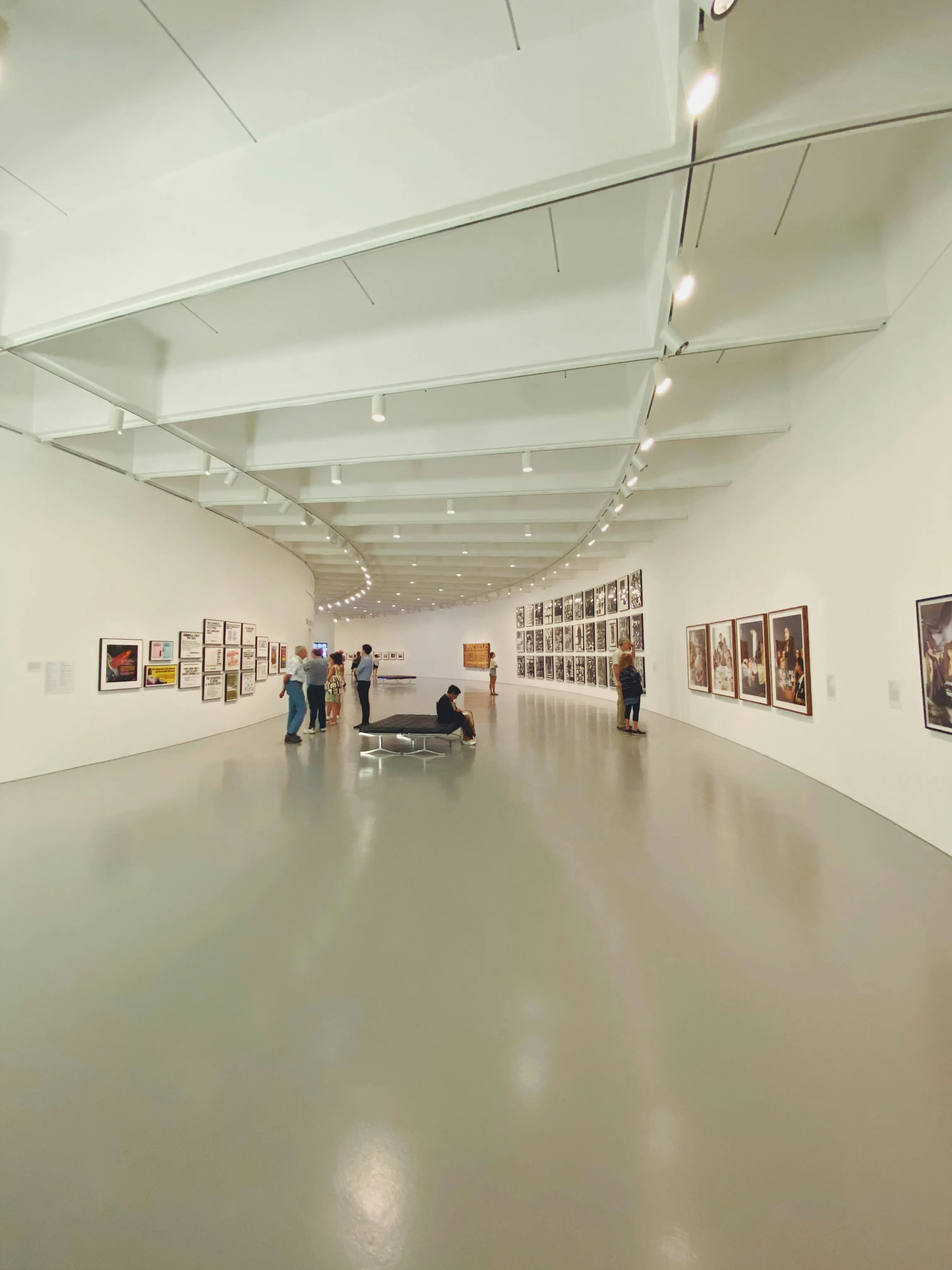 A visitor standing at the far end of a pale gallery wall hung with paintings
