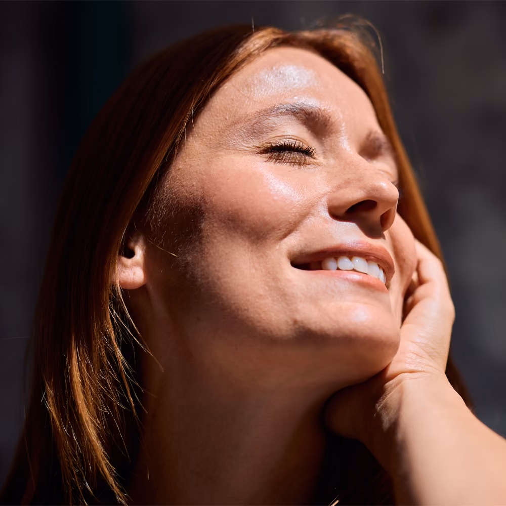 Lächelnde Frau mit natürlicher Hautstruktur im Sonnenlicht – Minimalinvasive Faltenbehandlung und Biostimulation bei Dr. med. Markus Mulica.