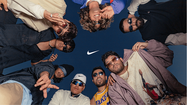 Group of eight diverse young men forming a circle looking down at the camera with a dark blue sky background and a white Nike logo in the center.