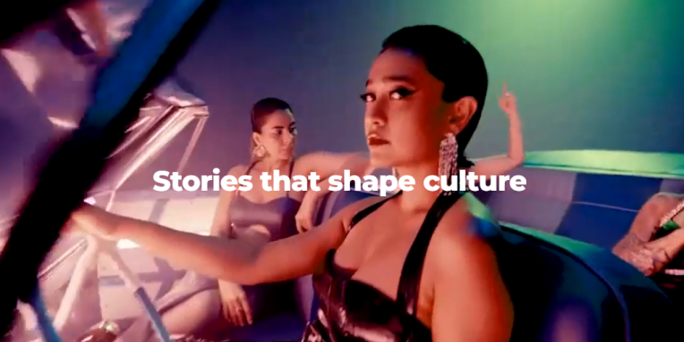 Three women sitting inside a car with colorful lighting, one in the foreground looking intently at the camera, text reading 'Stories that shape culture' overlayed in white.