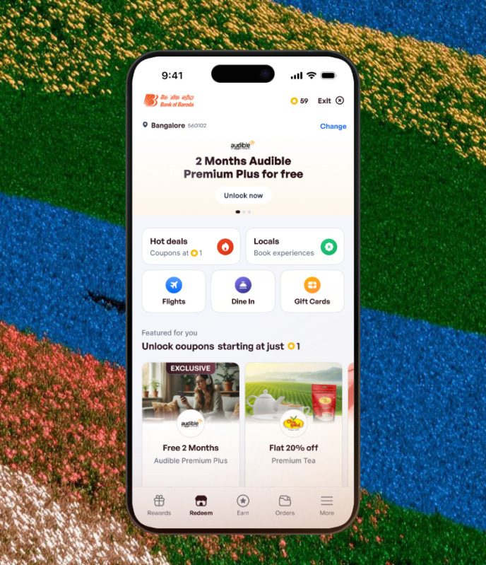 Mobile phone screen showing Bank of Baroda app with offer for 2 months of Audible Premium Plus free, options for hot deals, locals, flights, dine in, and gift cards, and featured coupons including free 2 months Audible Premium Plus and flat 20% off premium tea.