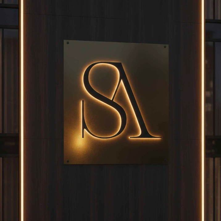 Illuminated metallic sign with stylized overlapping letters 'S' and 'A' on a dark wooden wall.