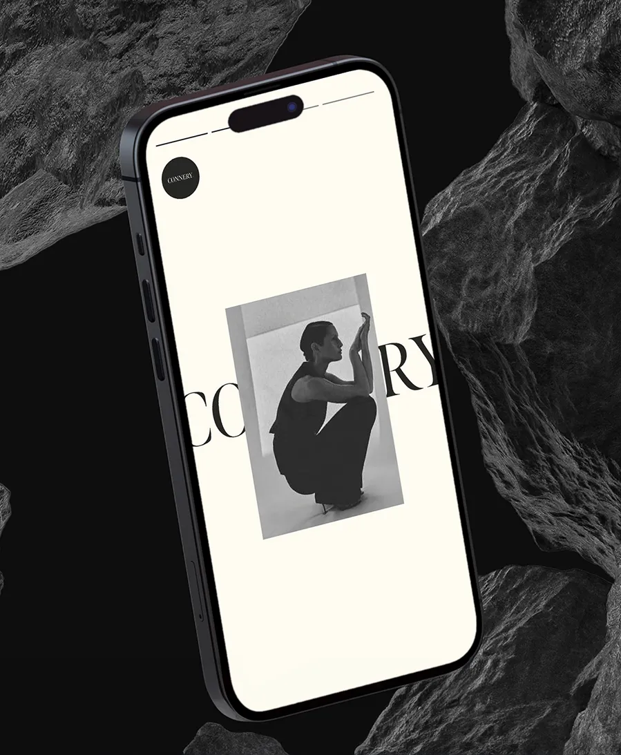 Black smartphone displaying a minimalist black and white fashion photo of a seated woman on a light background.