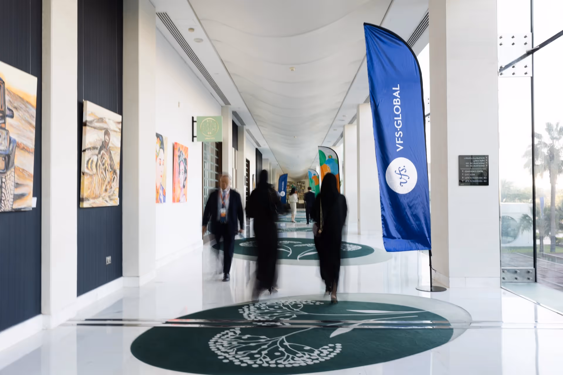 VFS Global event venue corridor with attendees, branded banners, artwork displays, and custom floor graphics.