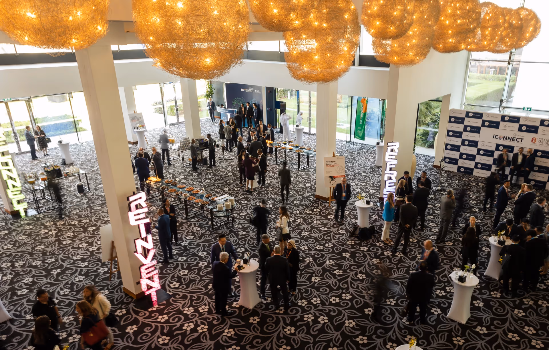 Attendees networking at the iCONNECT 8th Global Workshop, with catering stations, branded photo backdrop, and illuminated event installations in a spacious venue.
