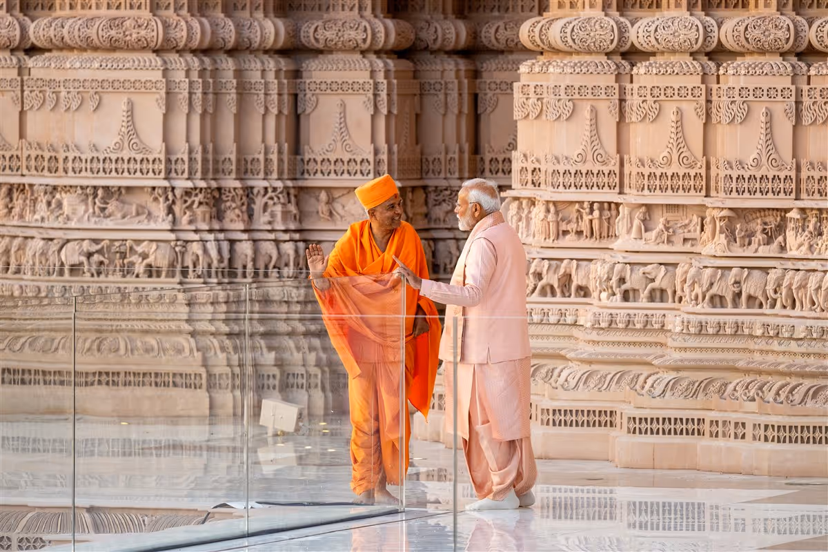 Two men standing inside an intricately carved Hindu temple, with ornate stone pillars, sculptures, and architectural details surrounding them.