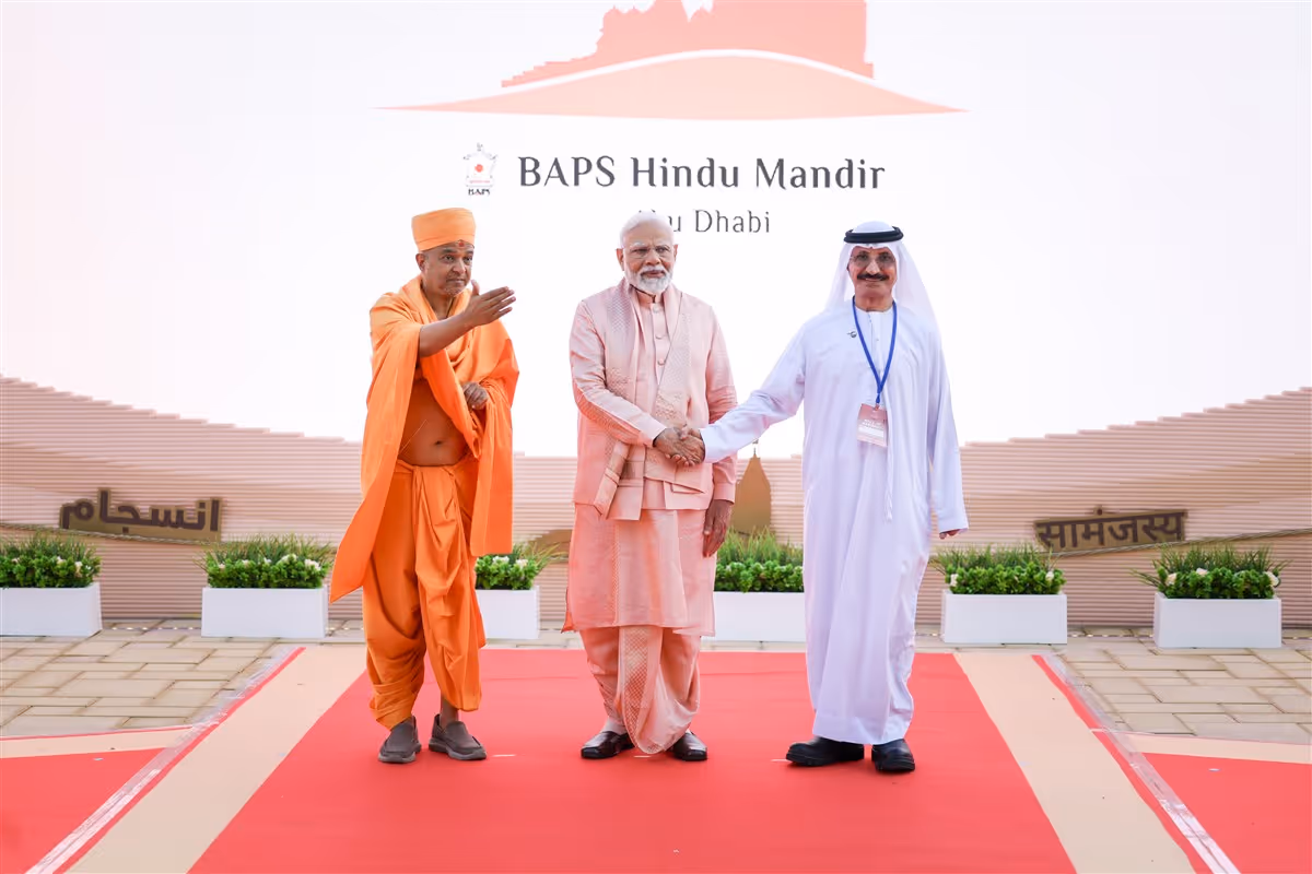 Three men standing on a red carpet outside the BAPS Hindu Mandir in Abu Dhabi, with the temple entrance and signage visible in the background.