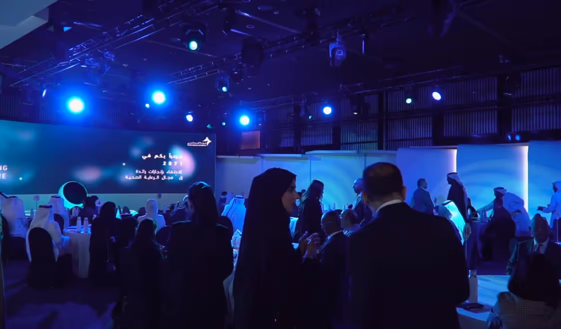 Guests networking at a formal Dubai Health Authority healthcare event under blue lighting.