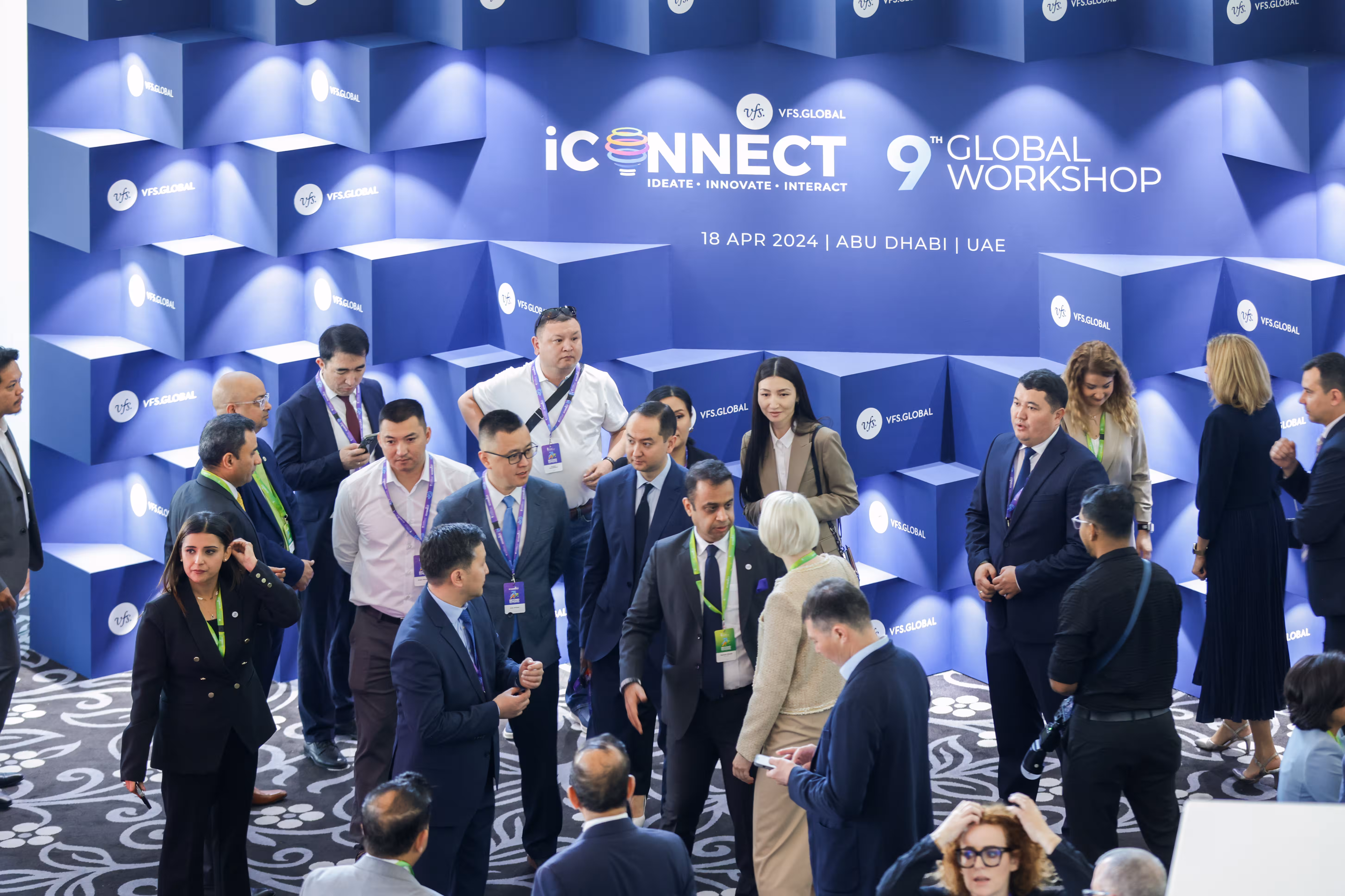Attendees networking and registering at a corporate conference, with an event reception desk and branded backdrop in the background.