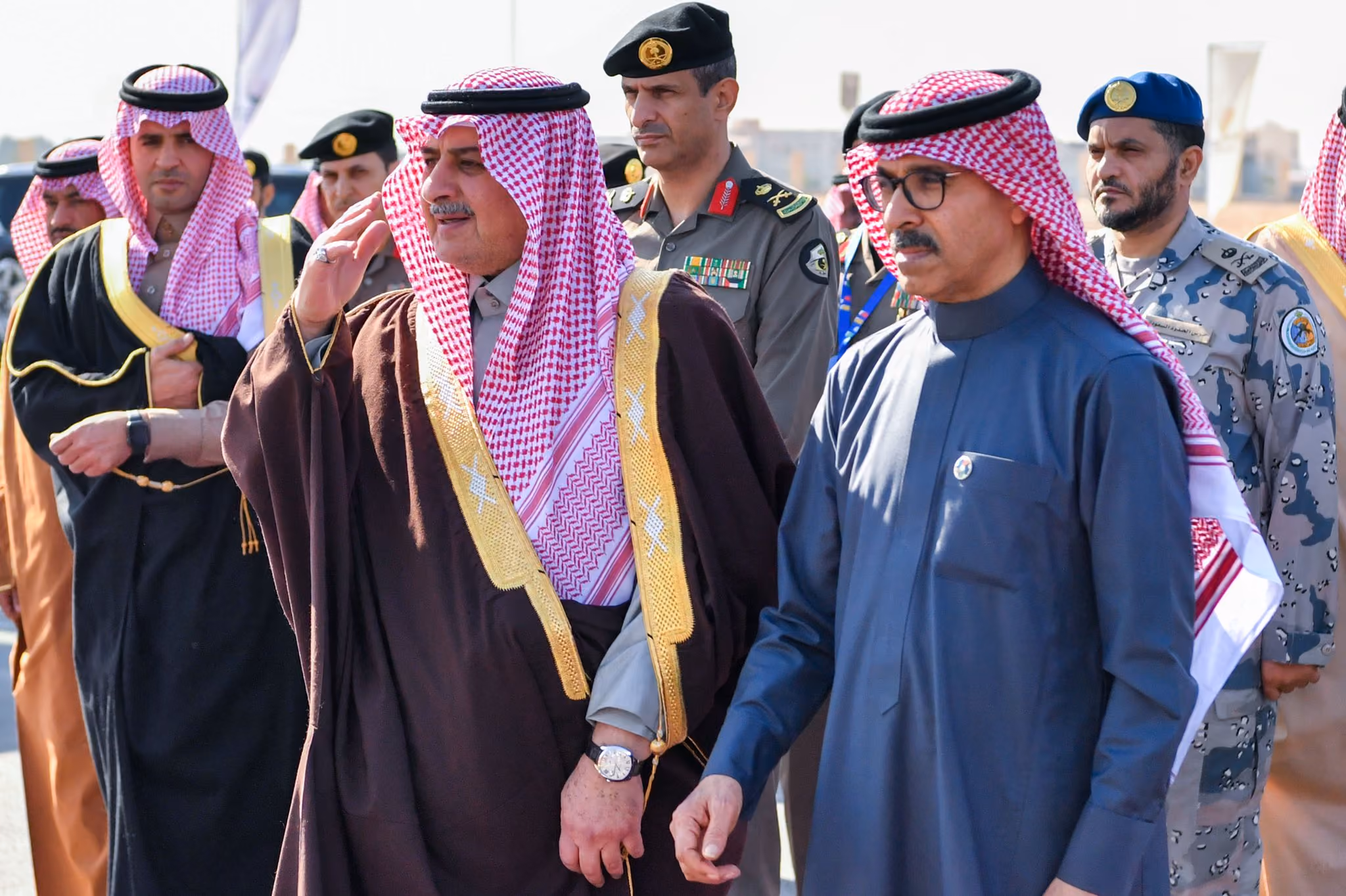 Middle Eastern officials and military personnel walking together outdoors, with several men wearing traditional attire and military uniforms.