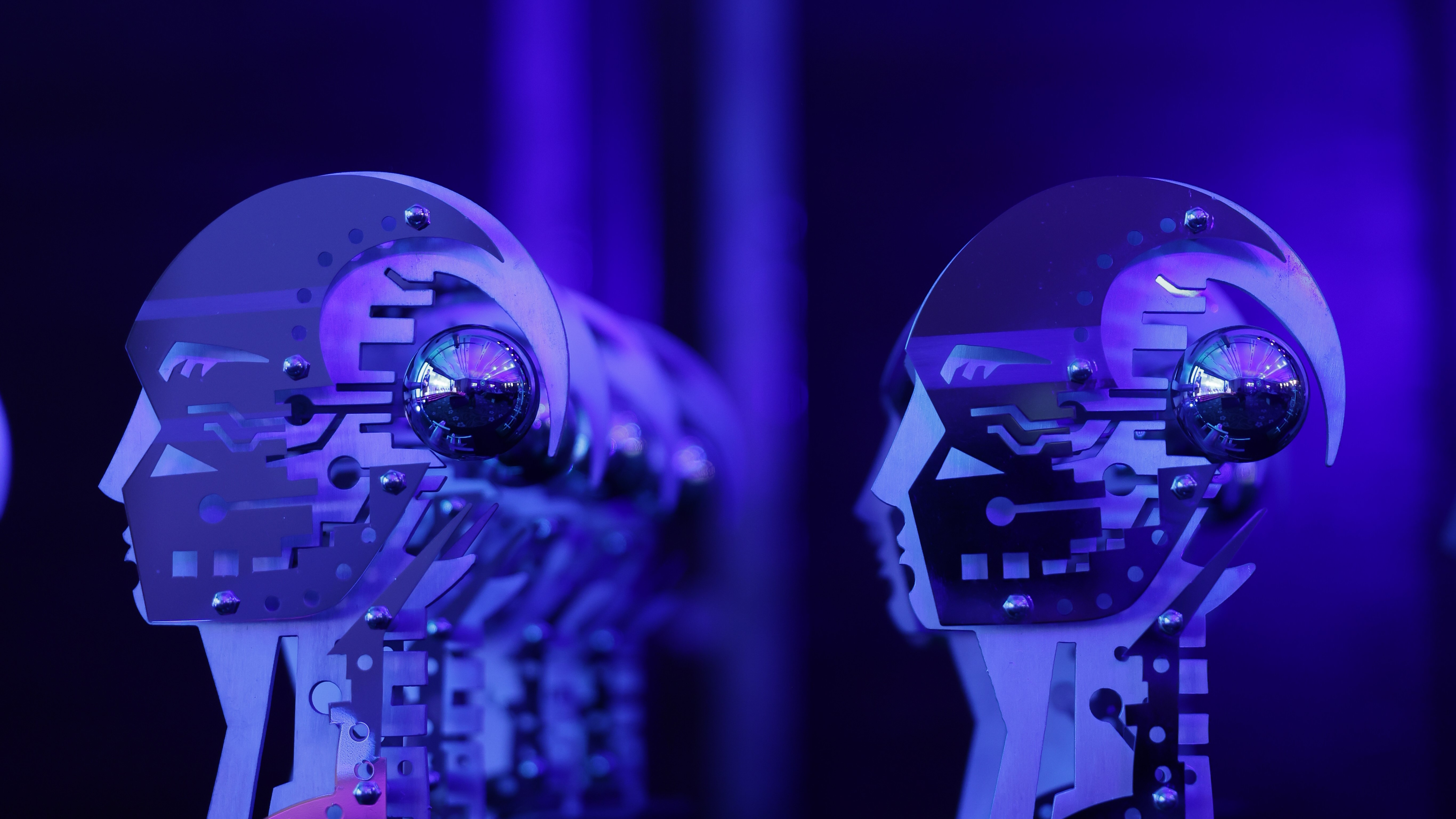 Futuristic robot face sculptures illuminated by blue and purple lighting at an immersive technology exhibition.