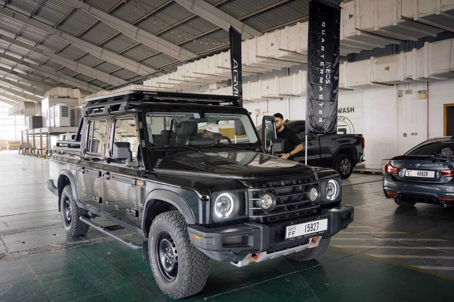 Black off-road SUV displayed inside an automotive service facility, with other vehicles and AGMC branding visible in the background.