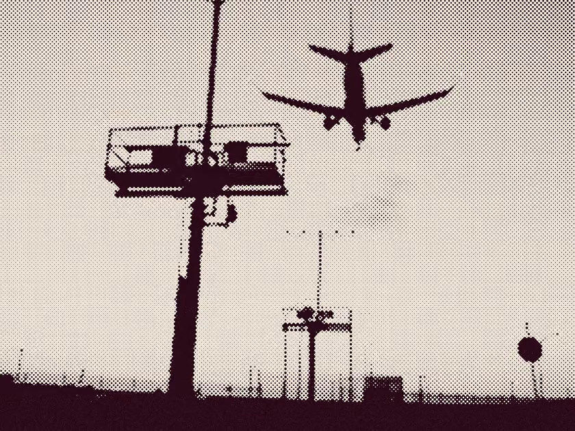 Silhouette of an airplane flying over airport runway lights against a pale sky.