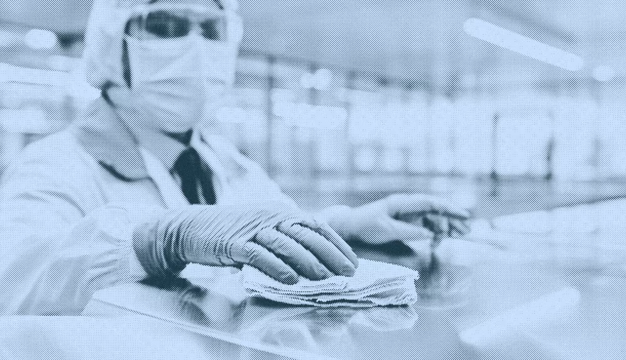 Person wearing protective gloves and mask wiping a surface with a cloth in a lab or cleanroom.