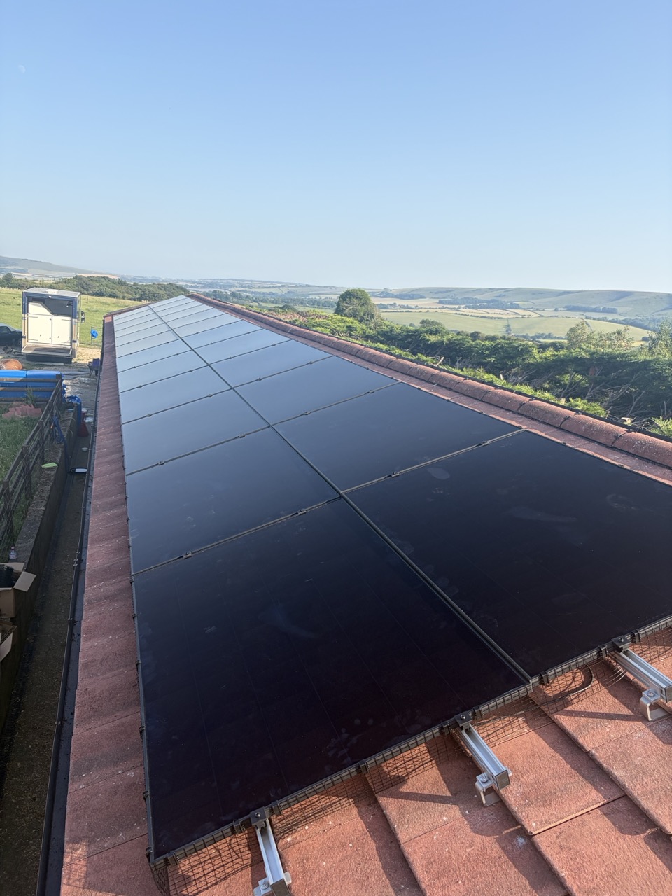 All-black solar panels fitted along a tiled roof, with open countryside beyond.