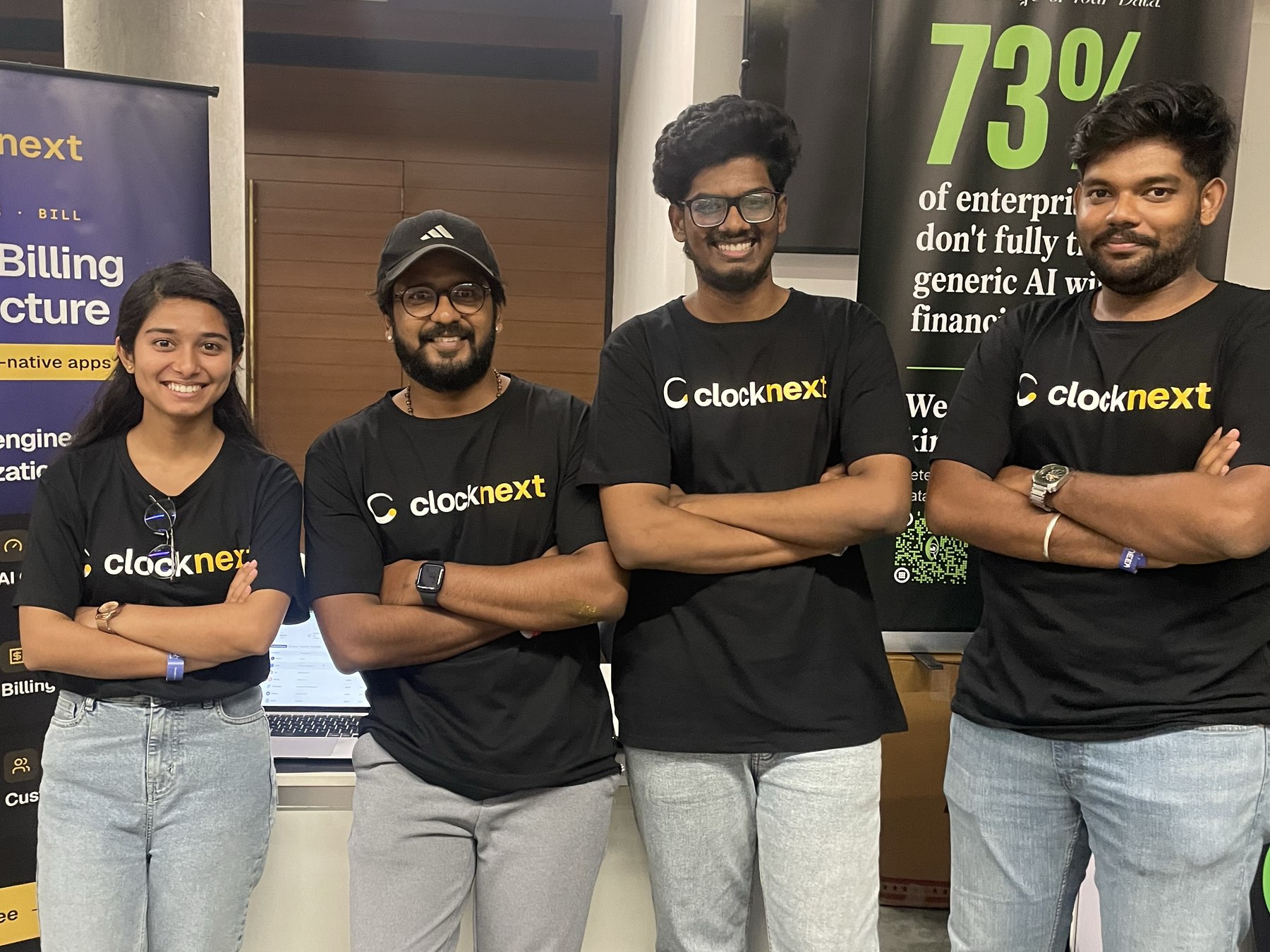 Four members of the Clocknext team standing together in Clocknext t-shirts beside the booth banner.