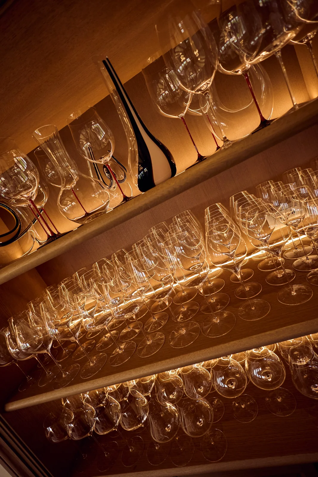 Lit shelves of stemware and decanters, restaurant photography for a fine dining venue