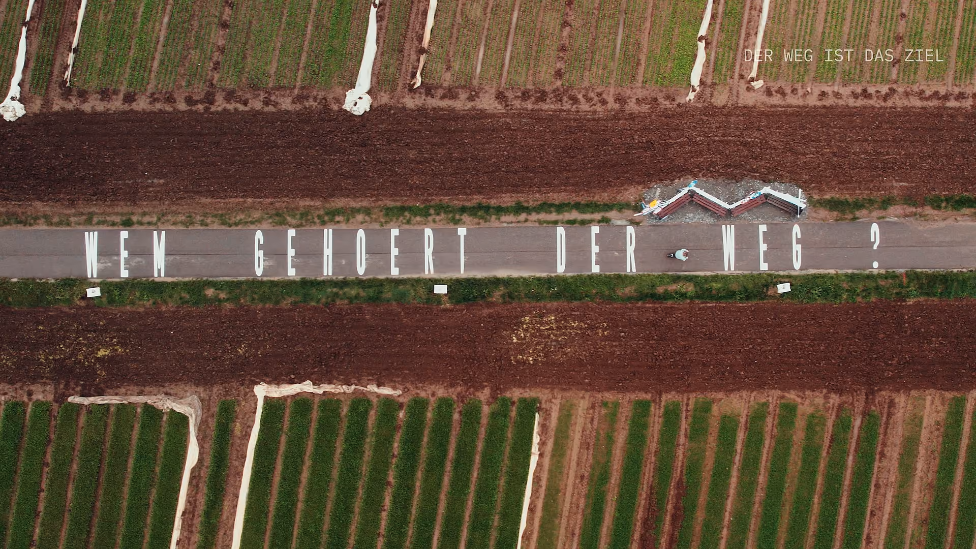 Aerial view of a pathway with large white letters spelling a German question in a field.