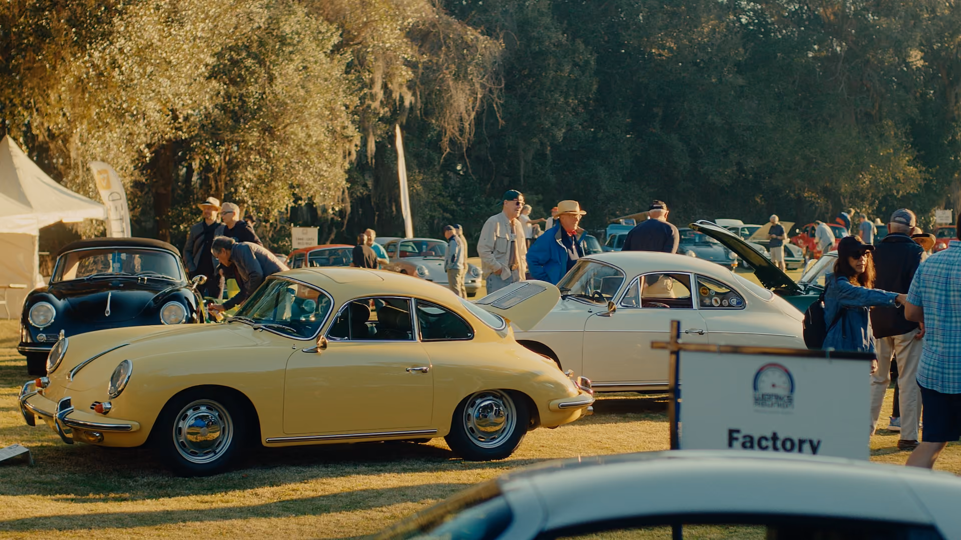Vintage cars displayed outdoors with people walking and inspecting them on a sunny day.