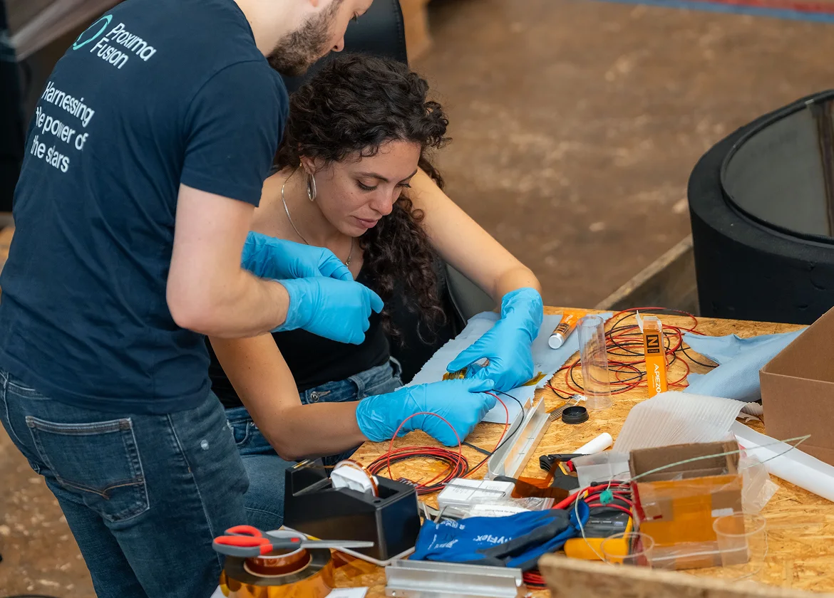 Several of Proxima Fusion's engineers wearing gloves, working on some electrical wires.