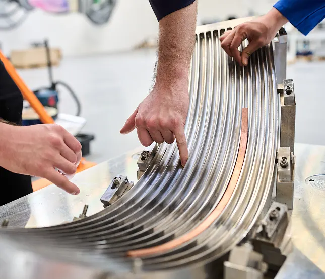 Several hands pointing at different grooves on an engineered piece of metal.