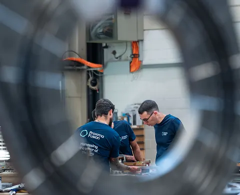 Two Proxima Fusion employees seen through a ring of wires.