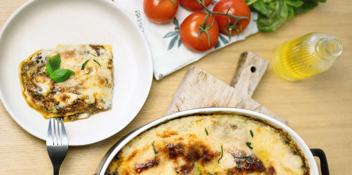 Part de lasagnes gratinées sur assiette, entourée de tomates cerises et de basilic frais