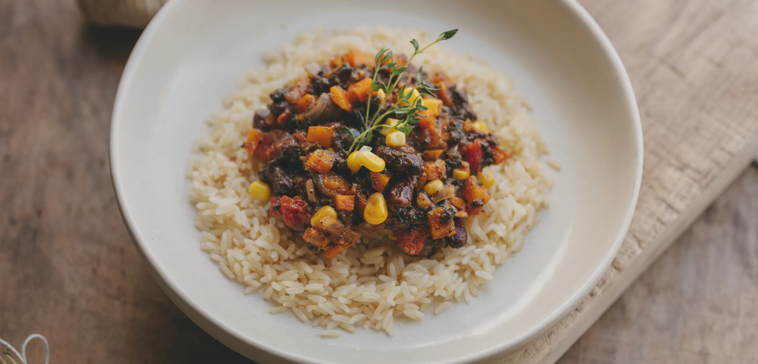 Chili sin carne préparé avec Edo sur lit de riz, garni de maïs, haricots rouges et thym, dans une assiette sur table en bois
