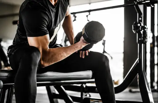 Man performing a seated dumbbell curl during a strength training workout in a gym.