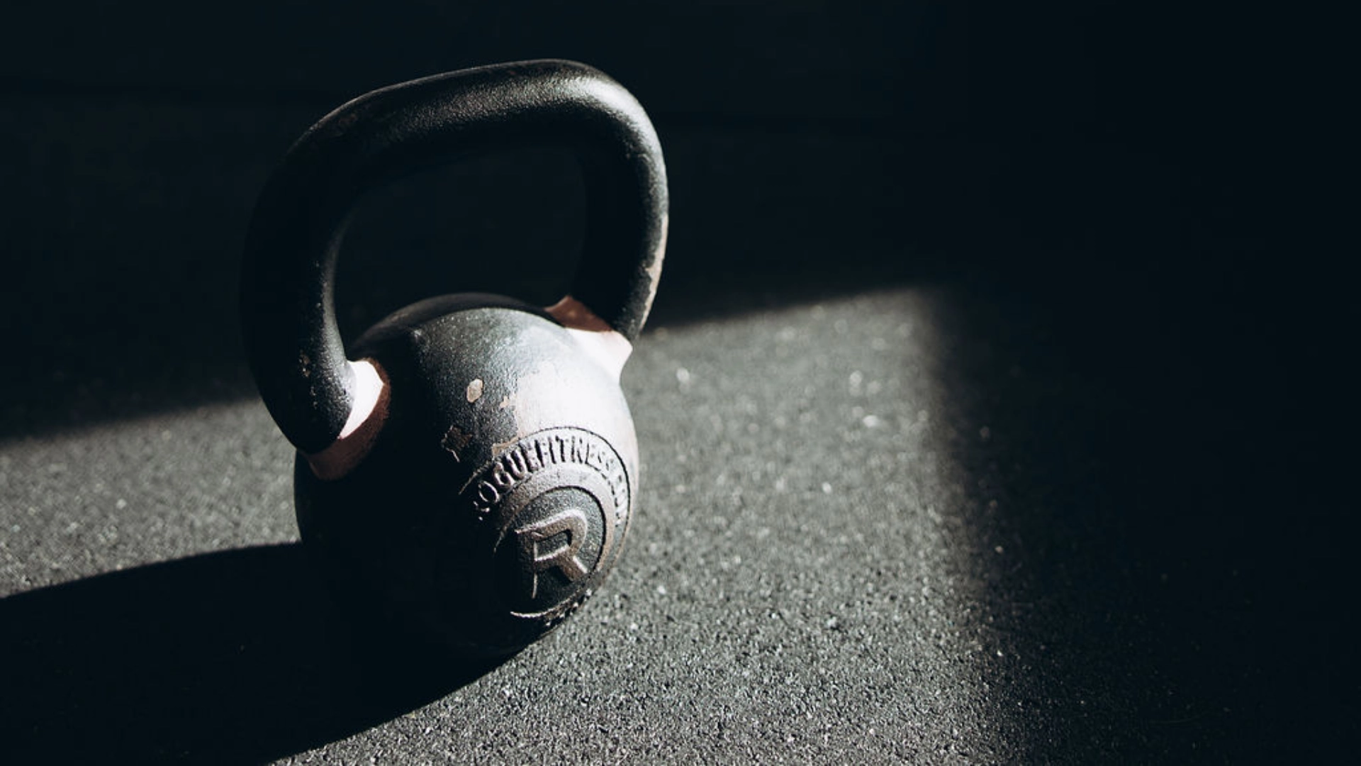 Kettlebell resting on a gym floor in dramatic natural light.