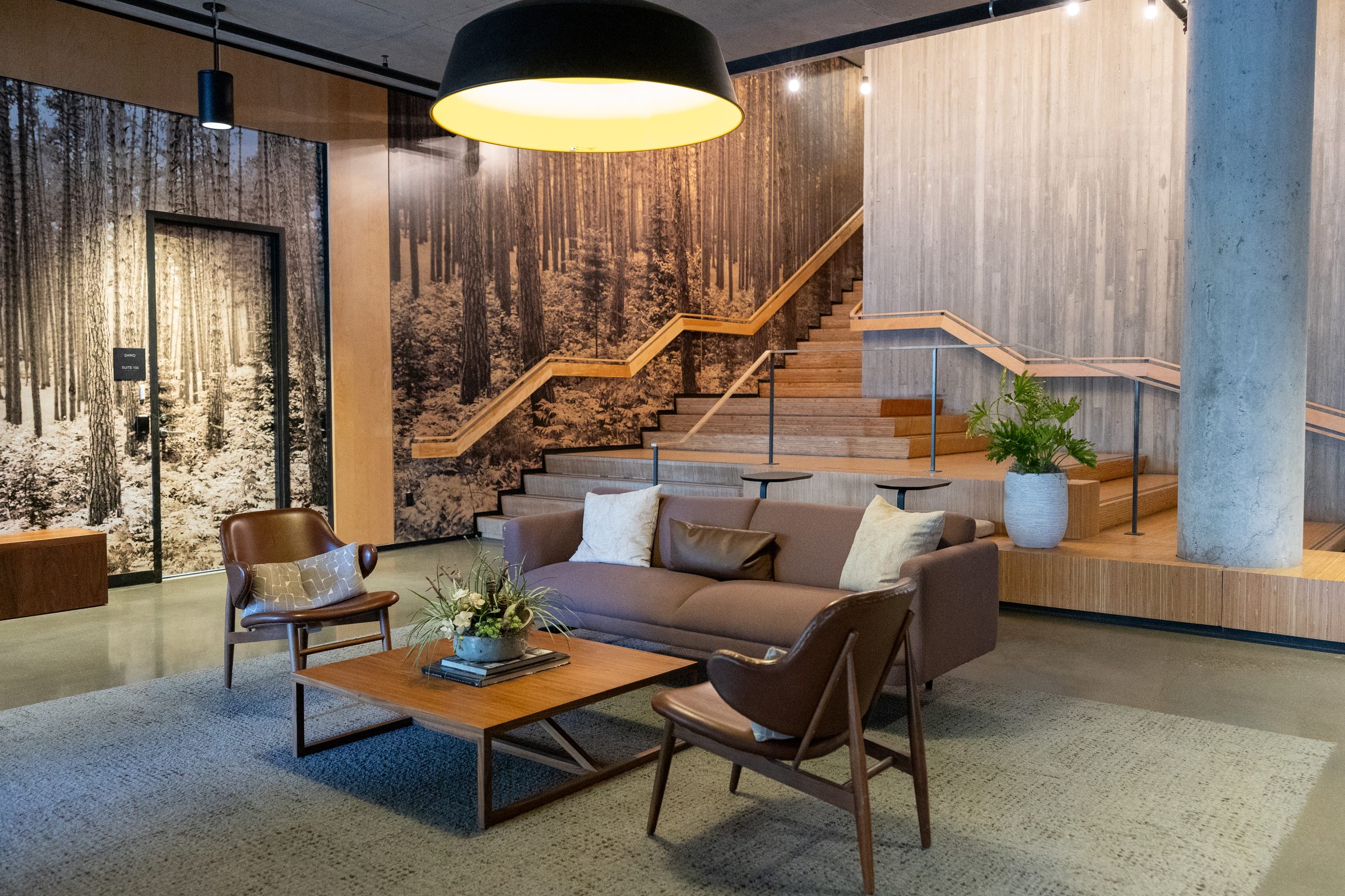 Lounge seating in a wood-lined office with a forest mural and stair