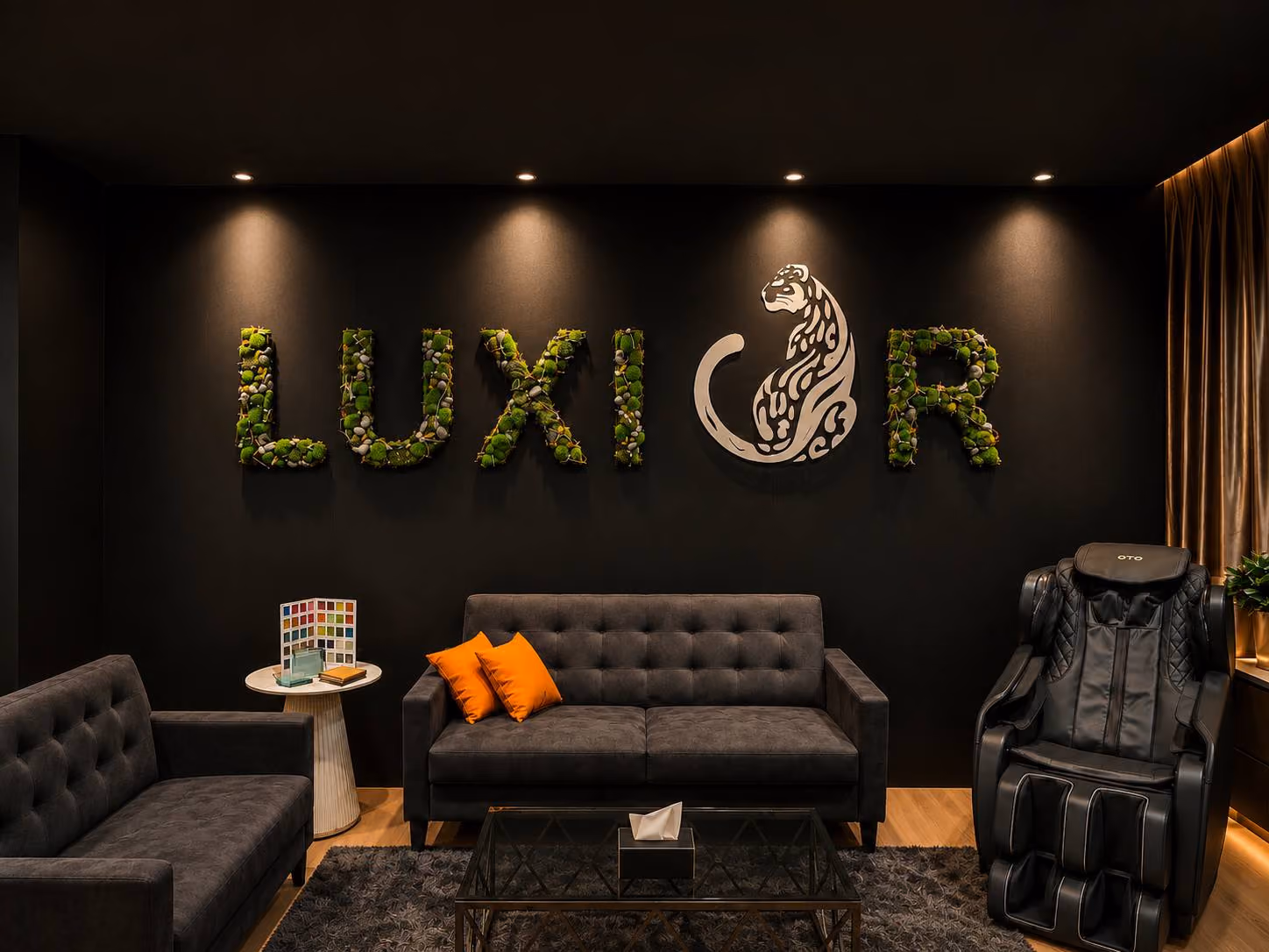 Luxior showroom lounge with dark sofas, a massage chair and a green Luxior wall sign.
