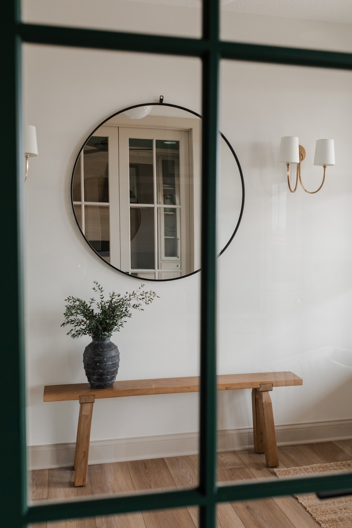 Entry with round mirror, brass sconces and oak bench