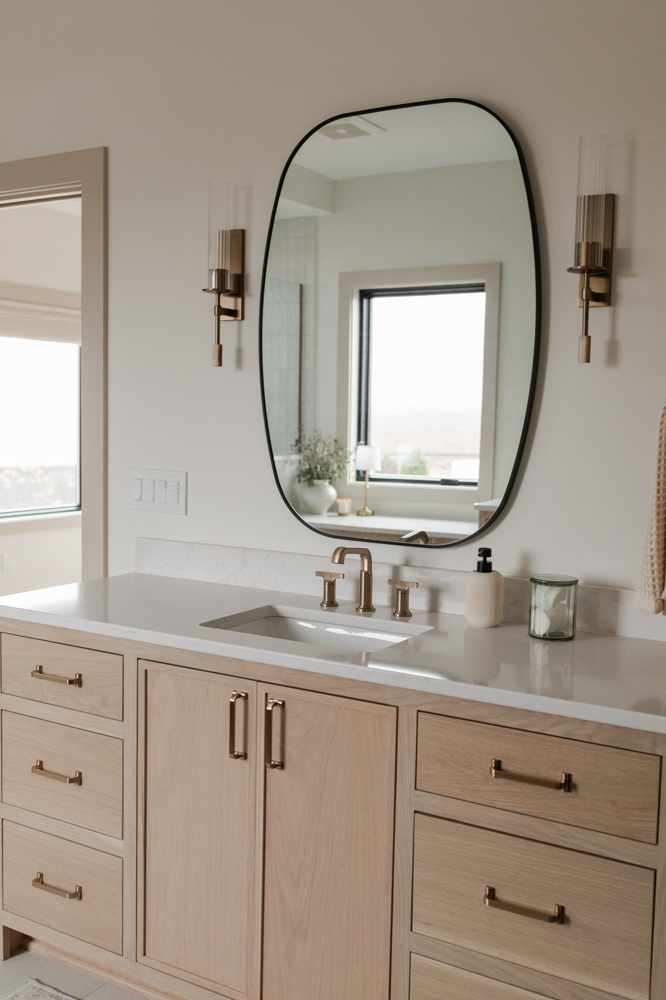 Primary bath vanity with white oak cabinetry and shaped mirror