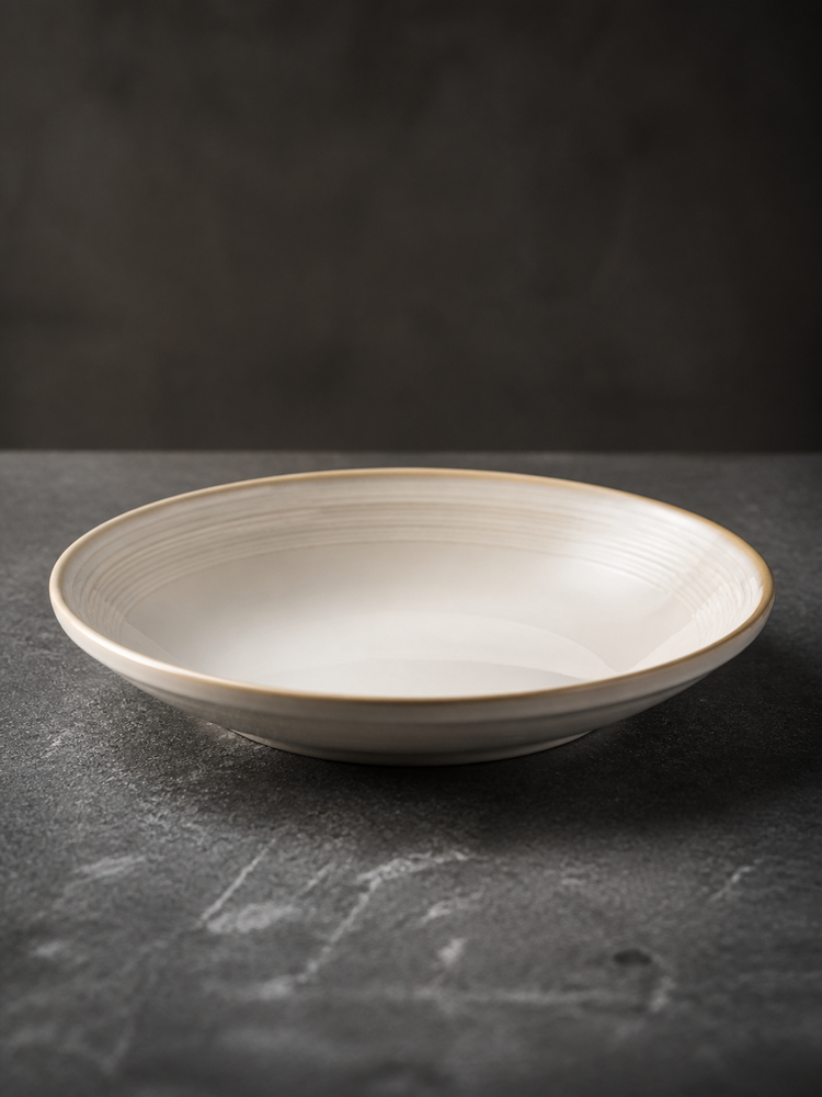 Close side view of a Quiet Rings wide-rim deep plate showing concentric line detail and a warm brown edge