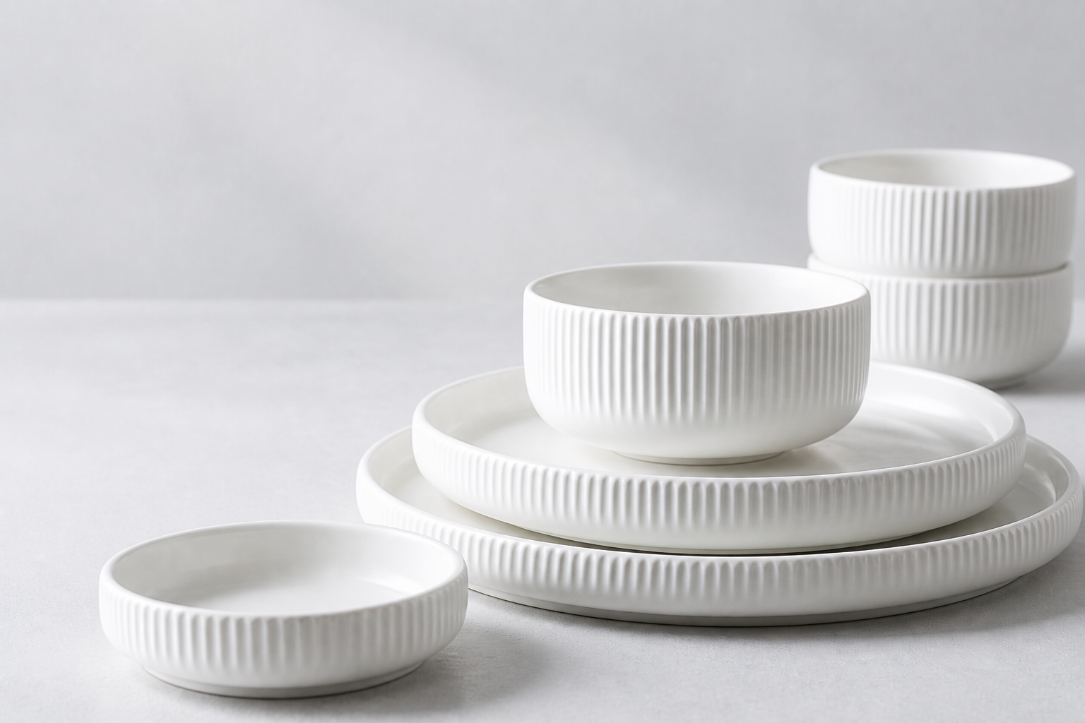 Soft Horizon warm-white ribbed ceramic plates and bowls arranged as a coordinated collection